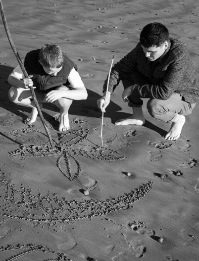 Photo of two youths drawing in the sand at a beach